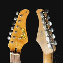 Close-up of two guitar heads with 'Cort' branding on a black background