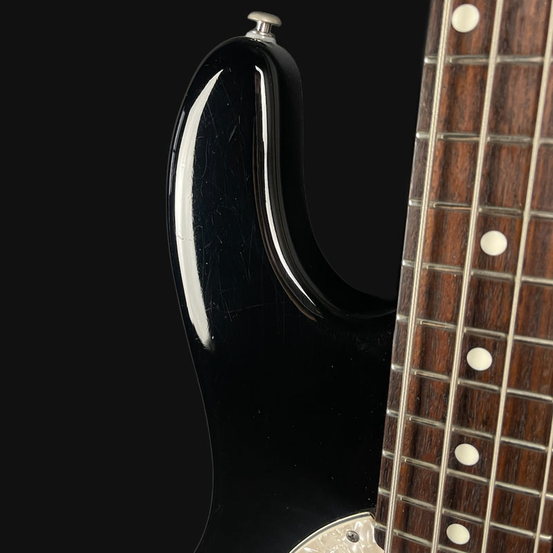 Close-up of a black electric guitar with a wooden neck on a black background