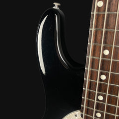 Close-up of a black electric guitar with a wooden neck on a black background