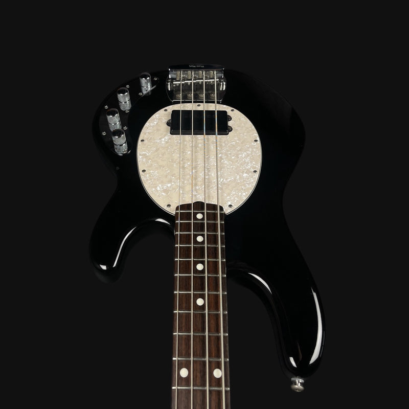 Black electric bass guitar with a white pickguard on a black background