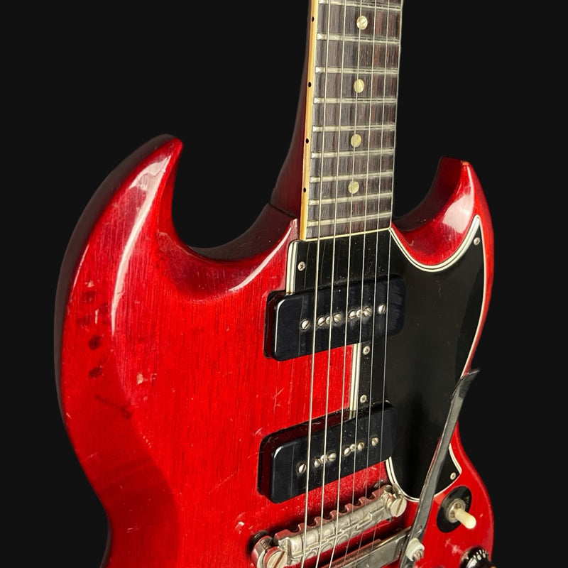 Red electric guitar with a black pickguard on a black background