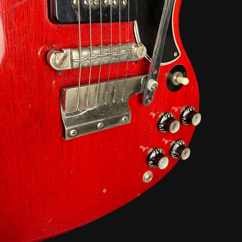 Close-up of a red electric guitar with a black pickguard on a black background
