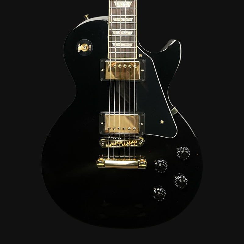 Black electric guitar with gold hardware on a black background