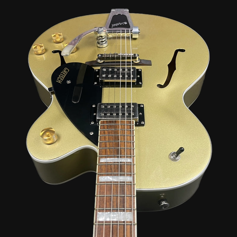 Gold electric guitar with a black pickguard on a black background