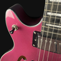 Close-up of a pink electric guitar with a black pickguard on a dark background