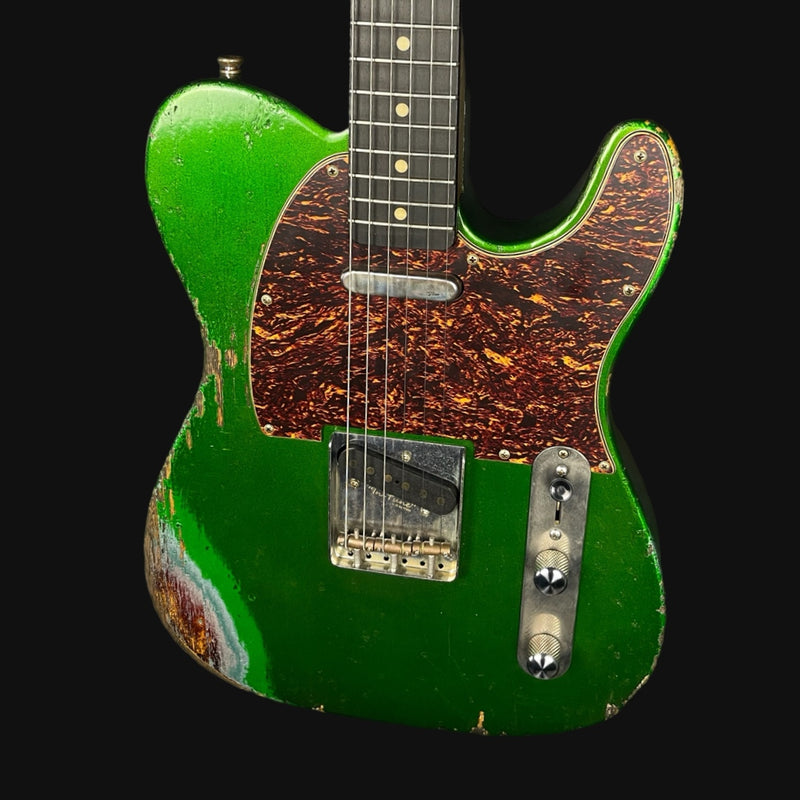 Green electric guitar with a worn finish on a black background