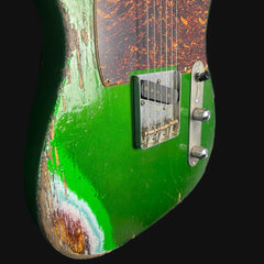 Close-up of a green electric guitar with a worn finish on a black background
