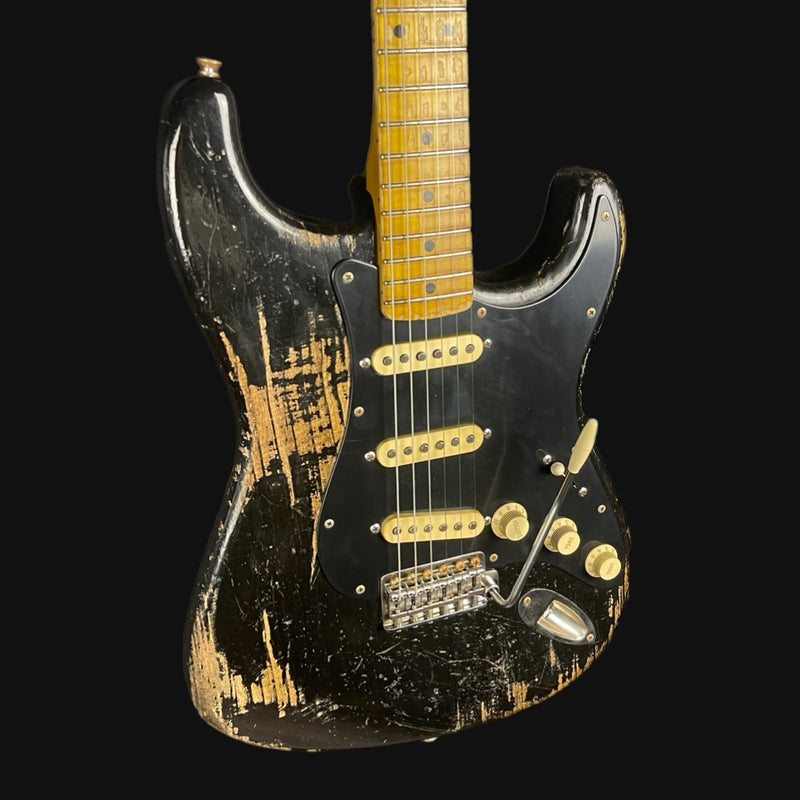 Worn electric guitar with a black and gold finish on a black background
