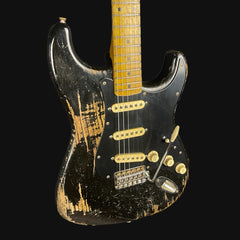 Worn electric guitar with a black and gold finish on a black background