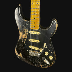 Worn electric guitar with a black and gold finish on a black background