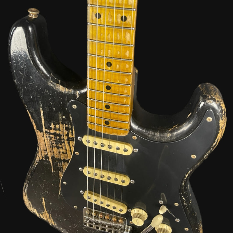 Worn black electric guitar with a yellow neck on a black background