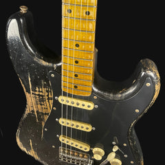 Worn black electric guitar with a yellow neck on a black background