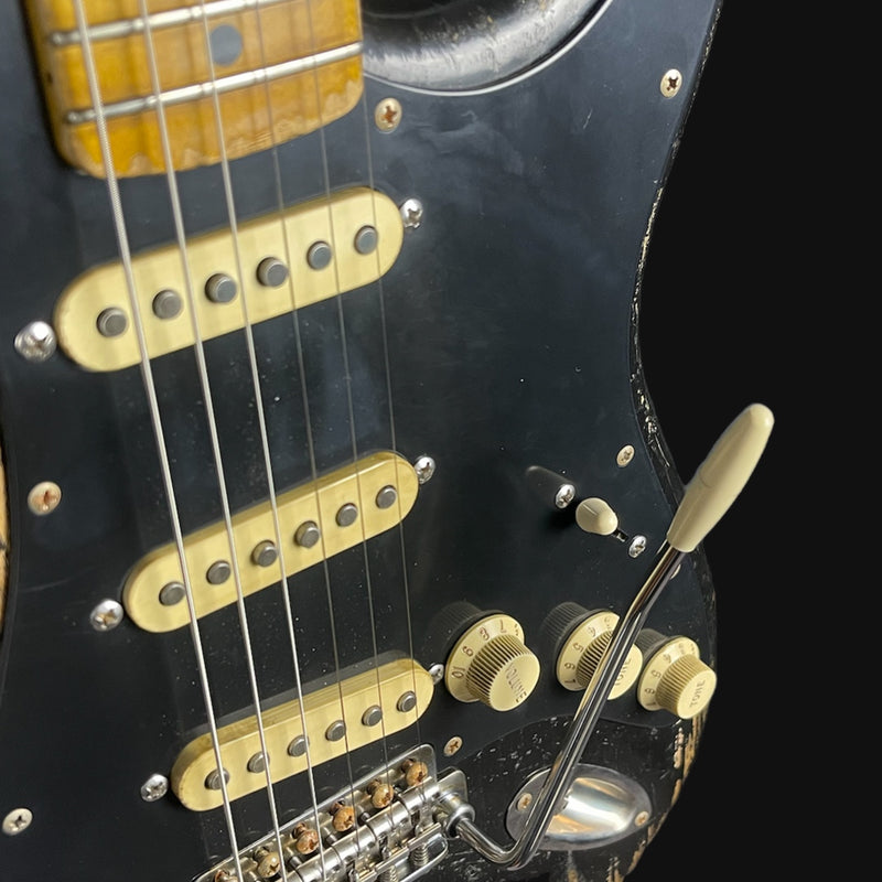 Close-up of a black electric guitar with gold hardware on a black background