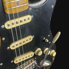 Close-up of a black electric guitar with gold hardware on a black background
