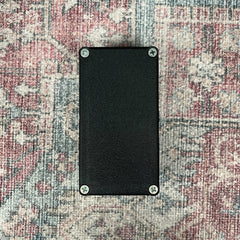 Black rectangular object with screws on a patterned fabric background