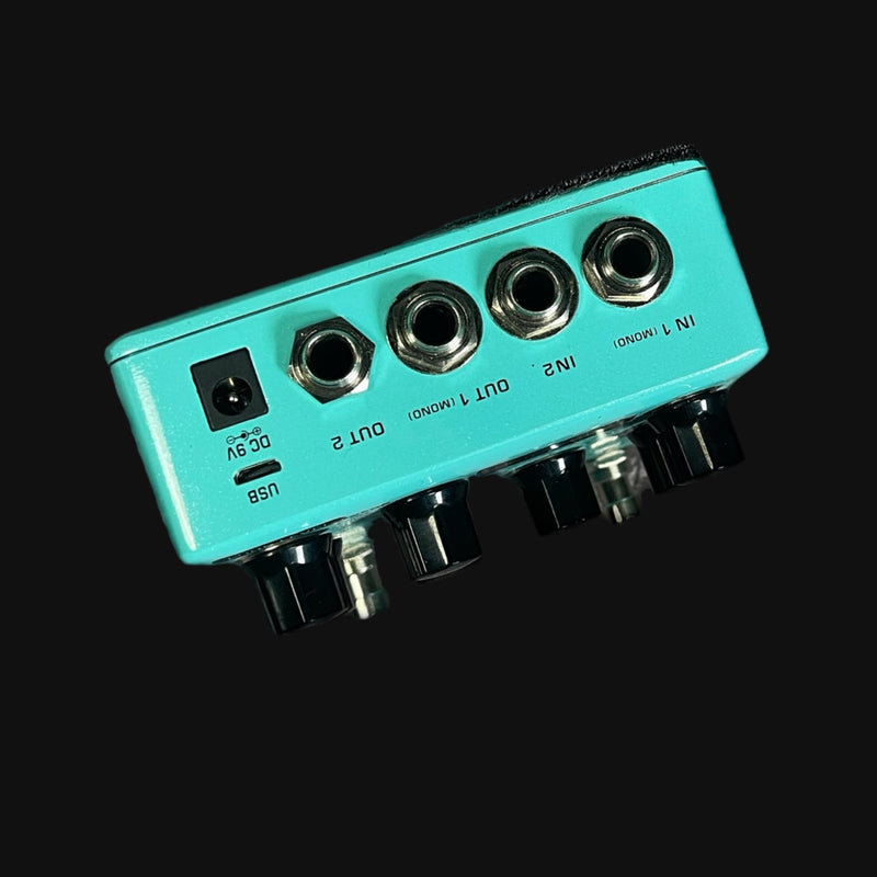Turquoise guitar effects pedal with multiple jacks on a black background