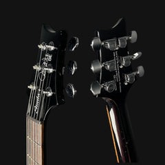 Close-up of a guitar's headstock with tuning pegs on a black background
