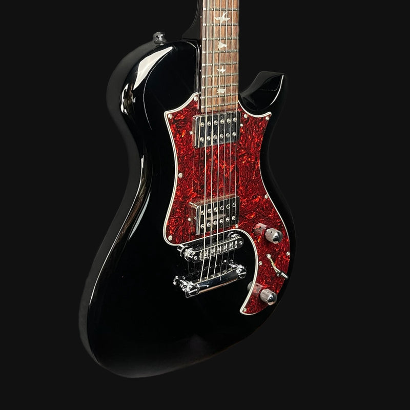 Black electric guitar with red glittery pickguard on a black background