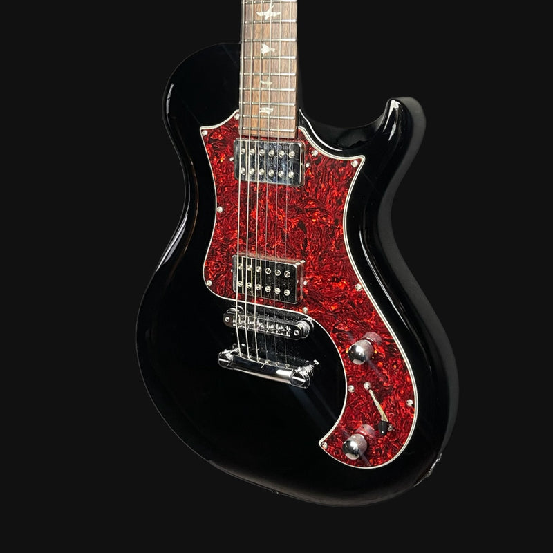 Black electric guitar with red glittery pickguard on a black background