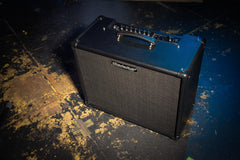 Black guitar amplifier with blue top on a worn wooden floor