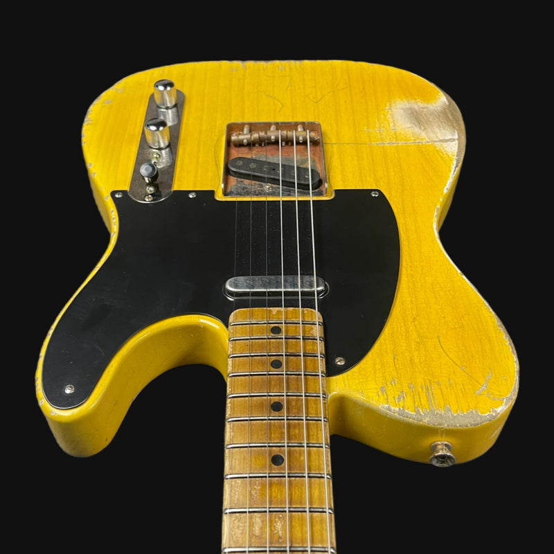 Yellow electric guitar with a black pickguard on a black background