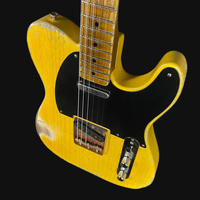Yellow electric guitar with a black pickguard on a black background
